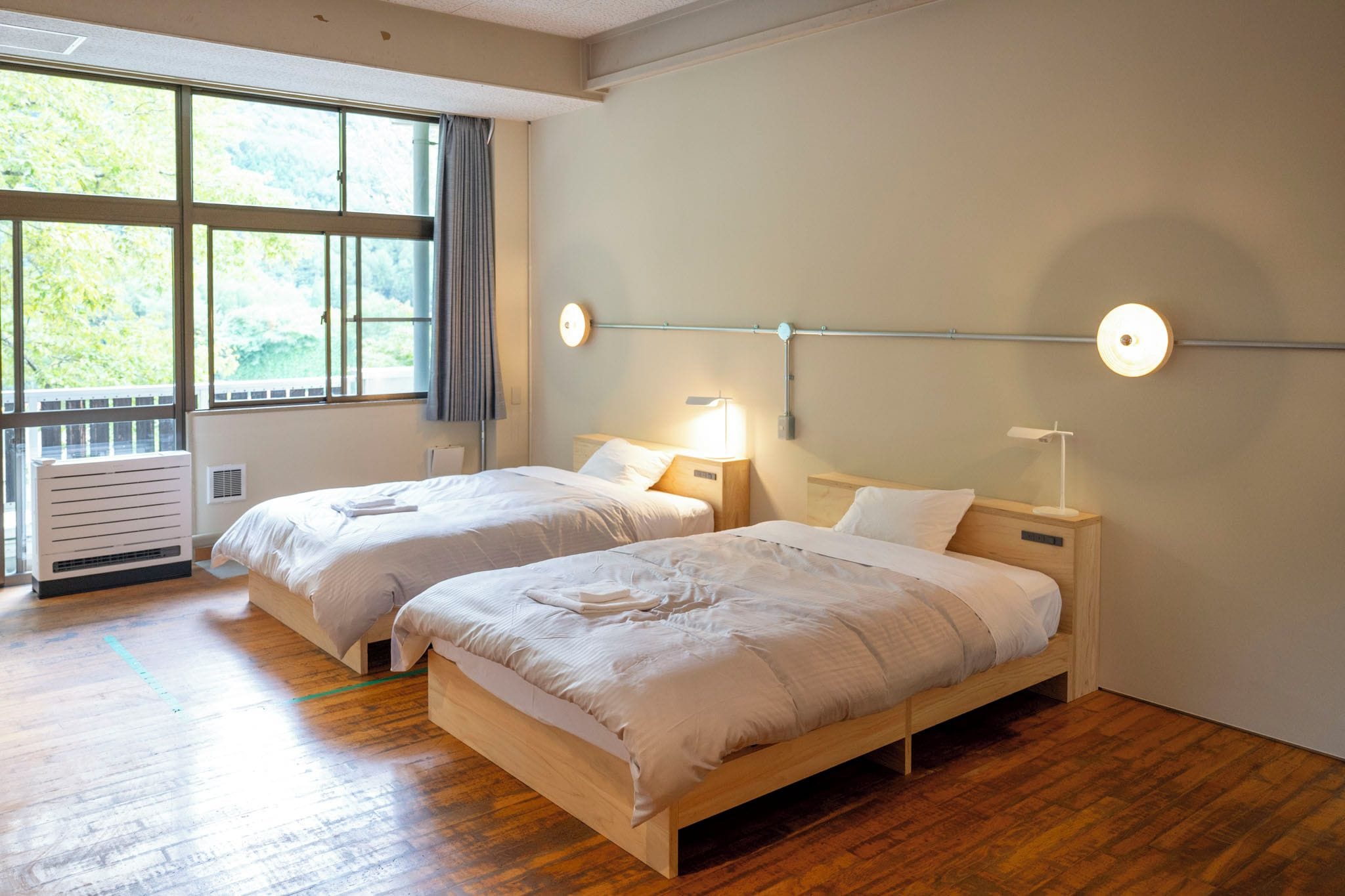 Ett hotellrum med två separata sängar, ett stort fönster med gardiner, ett element och sänglampor.