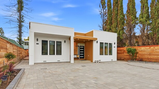 A modern two-story house with a paved driveway, large windows, and a wooden fence.