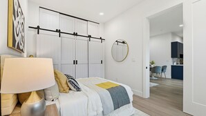 A modern bedroom with a bed, bedside lamp, and a view into the kitchen.