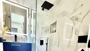A modern bathroom with a glass shower enclosure, marble walls, and a white toilet.