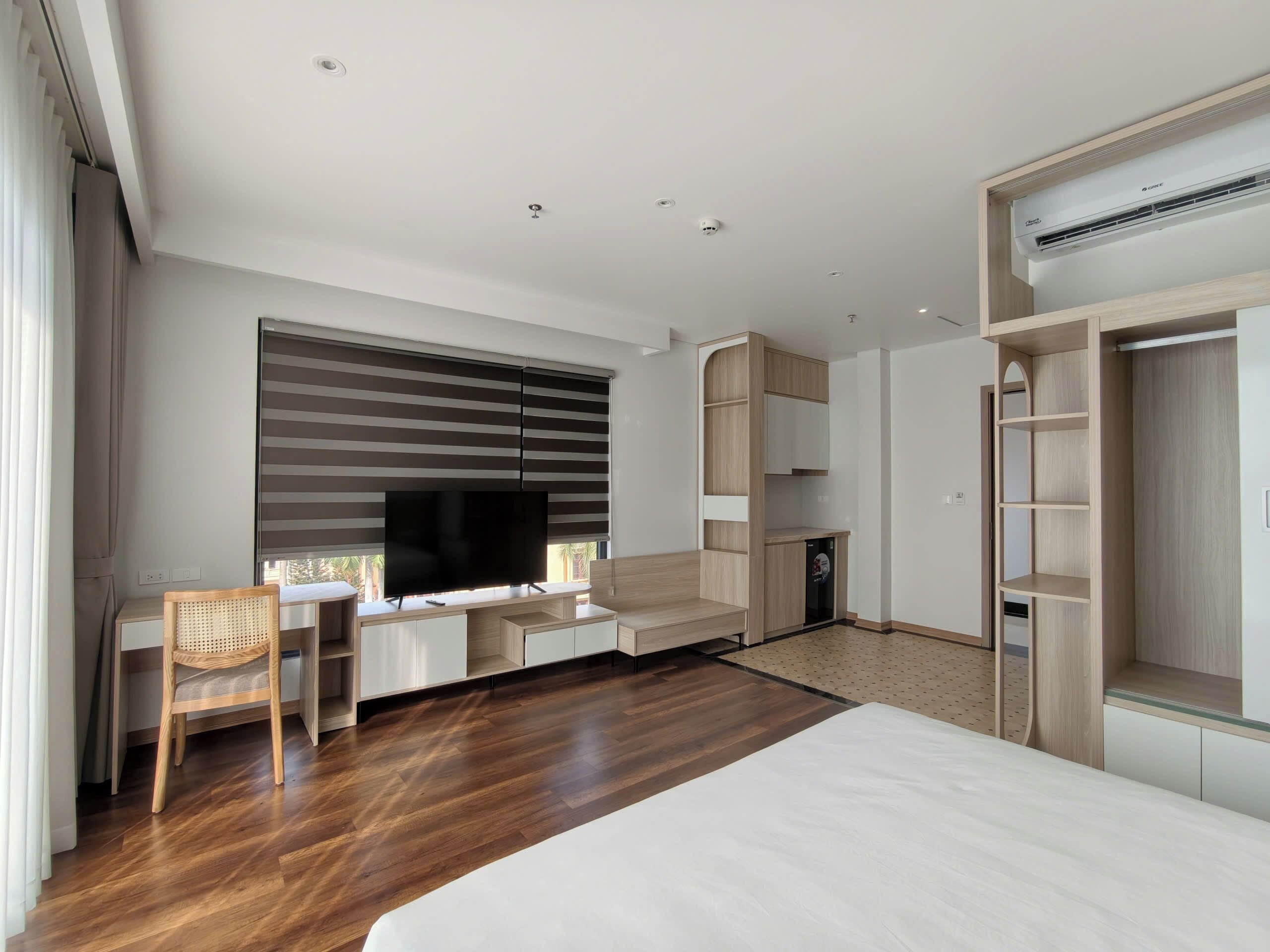 A modern hotel room with a large bed, a desk with a flat-screen TV, a wardrobe, and built-in shelving.