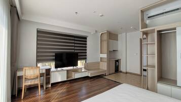 A modern hotel room with a large bed, a desk with a flat-screen TV, a wardrobe, and built-in shelving.