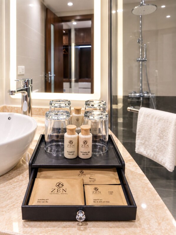 Baño con lavamanos, espejo y ducha. Hay una bandeja con artículos de aseo personal y un kit de afeitado.