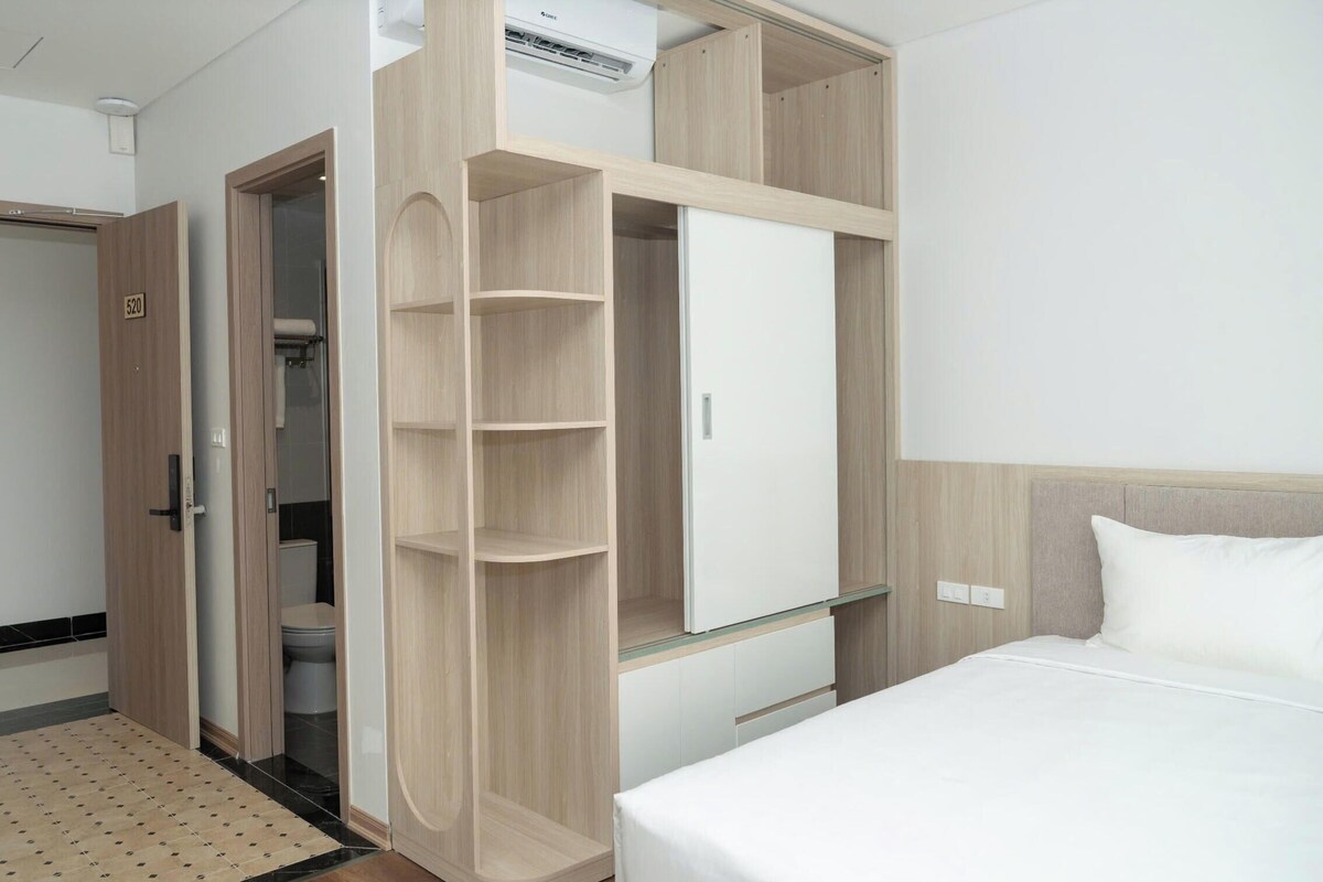 A hotel room with a bed, a wardrobe with multiple shelves, a bathroom, and an air conditioning unit.
