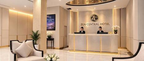 A hotel reception area with a reception desk, two receptionists, a large screen, and a modern interior design.