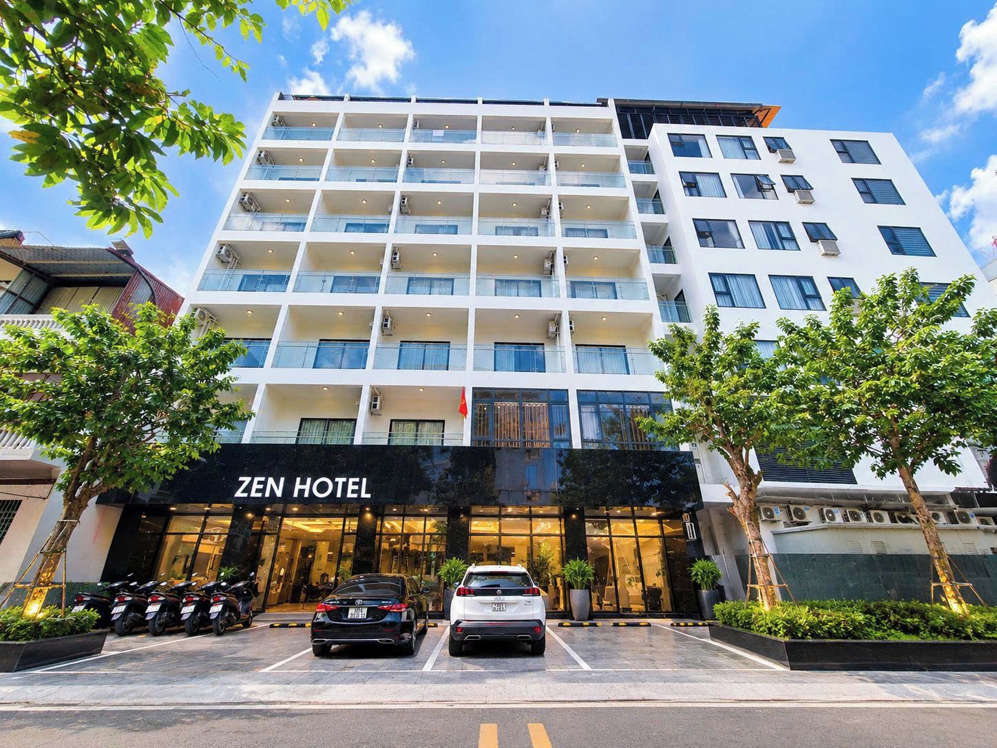 A multi-story hotel with a modern facade, a visible entrance, and a parking area with cars.