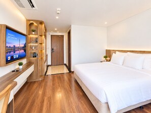 Una habitación de hotel con una cama, un televisor montado en la pared, un estante de madera con una planta y una puerta que conduce a otra habitación.