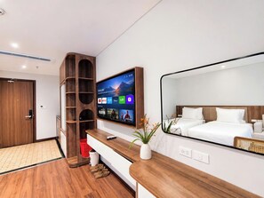 Habitación de hotel moderna con un televisor de pantalla plana grande montado en la pared, una mesita de noche de madera, una cama con ropa de cama blanca y una pequeña planta en maceta.