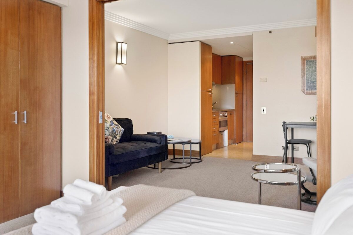 Een hotelkamer met een bed, een slaapbank, een klein tafeltje en een kitchenette op de achtergrond.