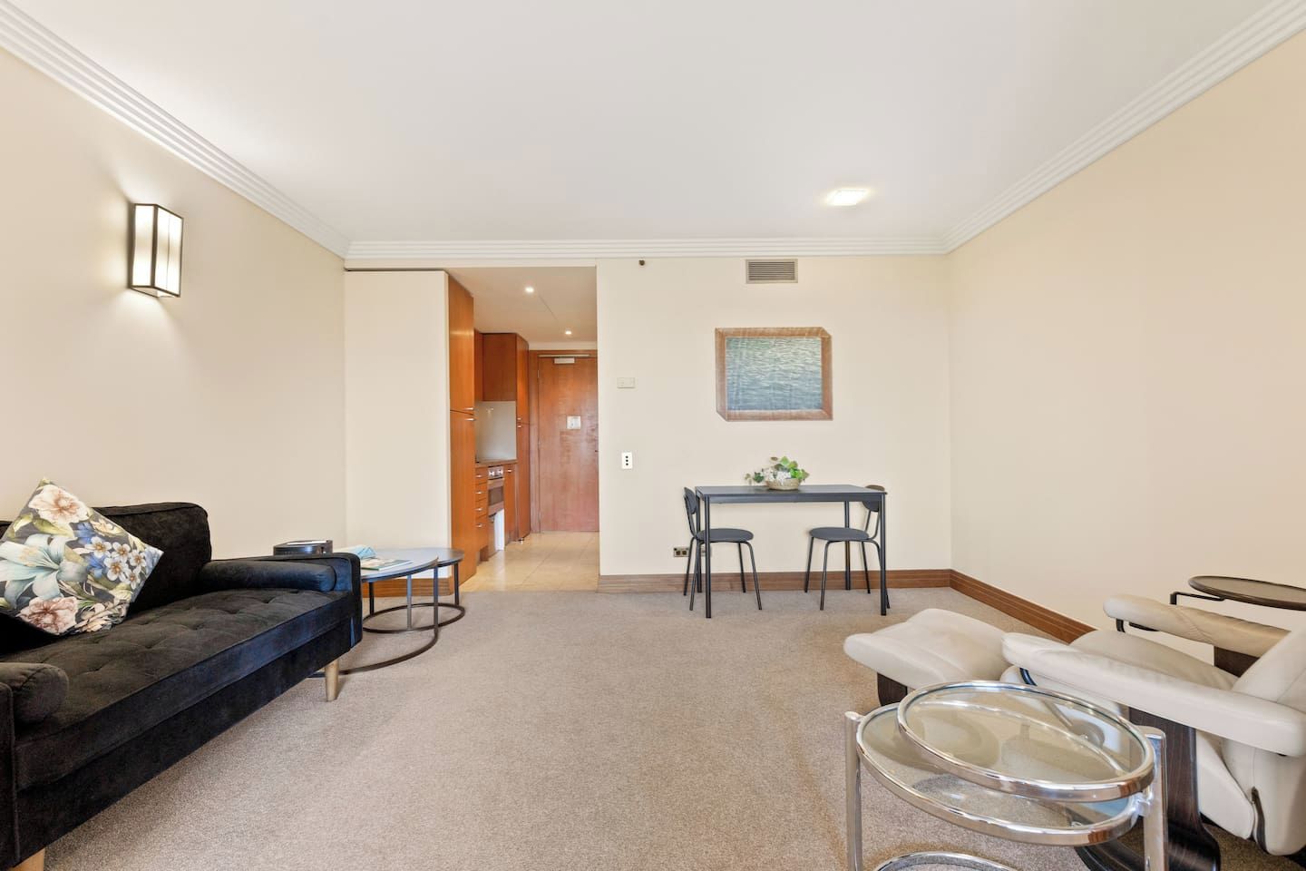 A living room with a sofa, a small table, a dining area with chairs, and a white armchair.