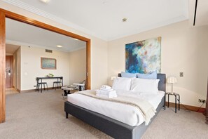A hotel room with a large bed, a desk with a chair, a painting on the wall, and a door leading to another room. - 1BR City Retreat with Pool & Gym Zodiak Stays (Auckland)