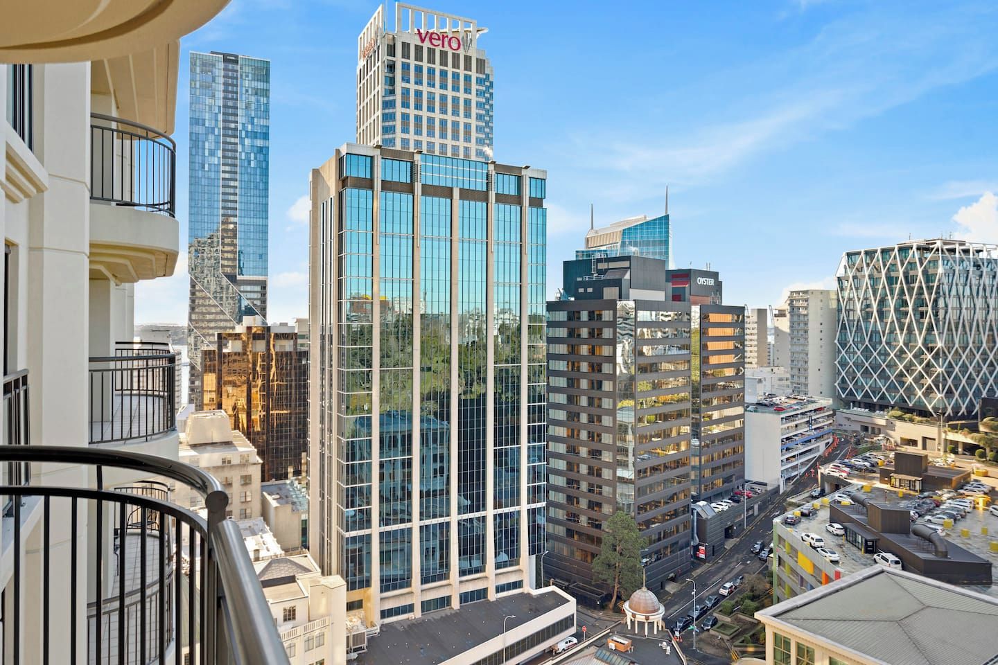 A high-rise building with a glass facade and a 'Vero' sign, surrounded by other modern buildings and a busy street below.