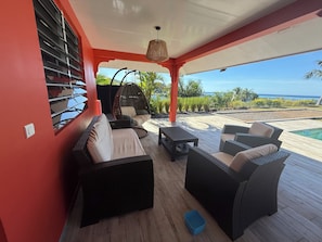 Un espacio al aire libre techado con mobiliario de mimbre, una silla colgante y vista al océano.