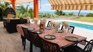 Zona pranzo all'aperto con vista sull'oceano, una piscina e una sedia a dondolo.