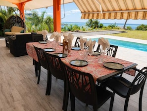 An outdoor dining area with a view of the ocean, a pool, and a hanging chair. - TE AVA (AVERA)