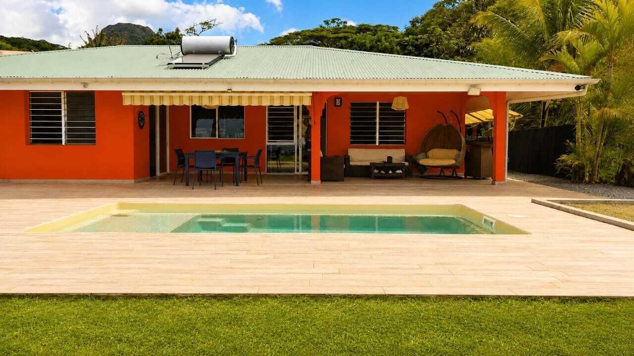 Une maison avec une piscine, un patio couvert et un petit espace extérieur aménagé pour s’asseoir.