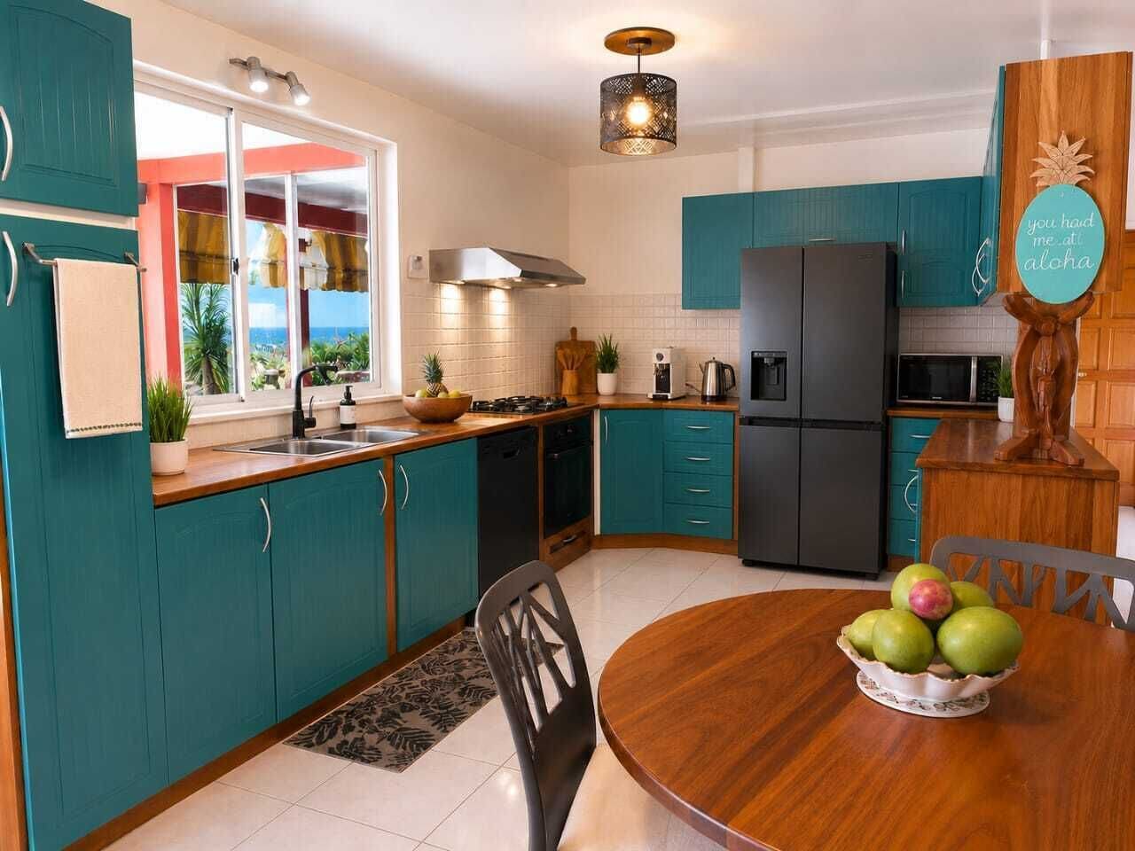 A kitchen with teal cabinets, a wooden dining table, and a fruit bowl.