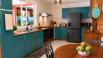 A kitchen with teal cabinets, a wooden dining table, and a fruit bowl.