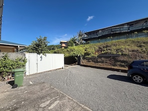 A parking area with a car, a white gate, and a green trash bin. - TE AVA (Raiatea)