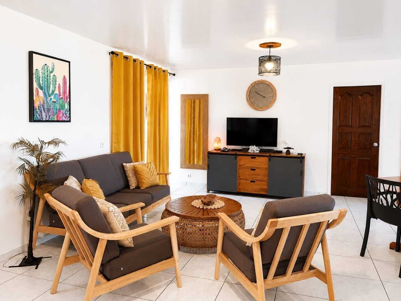 A living room with a sofa, two armchairs, a coffee table, a TV, and a wooden cabinet.