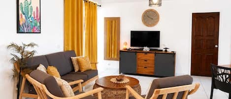 A living room with a sofa, two armchairs, a coffee table, a TV, and a wooden cabinet.