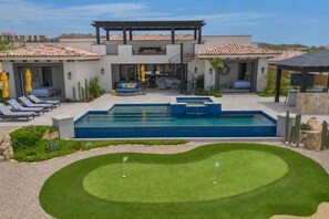 Un área de piscina moderna al aire libre con un campo de práctica de golf y sillones de descanso.
