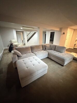 A spacious living room with a large L-shaped sectional sofa, a small table, and a staircase leading to an upper level.