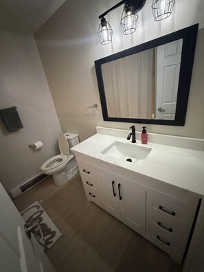 Un baño con lavamanos blanco, grifo negro y un espejo grande arriba.