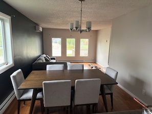 A dining room with a large table, four chairs, a sofa, and a chandelier.