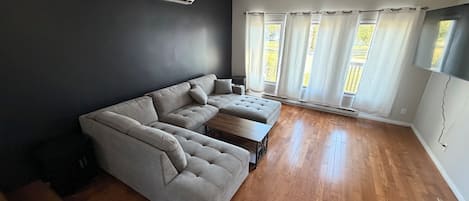 A living room with a sectional sofa, a coffee table, and a large window with curtains.