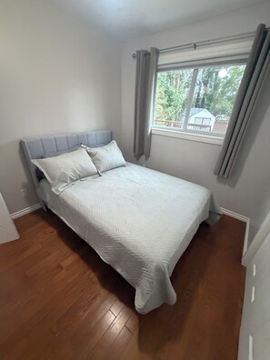 A bedroom with a bed, a window with curtains, and a view of a house outside.