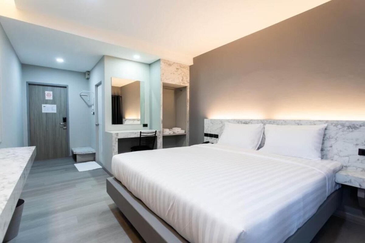 Una moderna camera d'albergo con un letto grande, un'area salotto, una toeletta con specchio e una porta con un cartello.