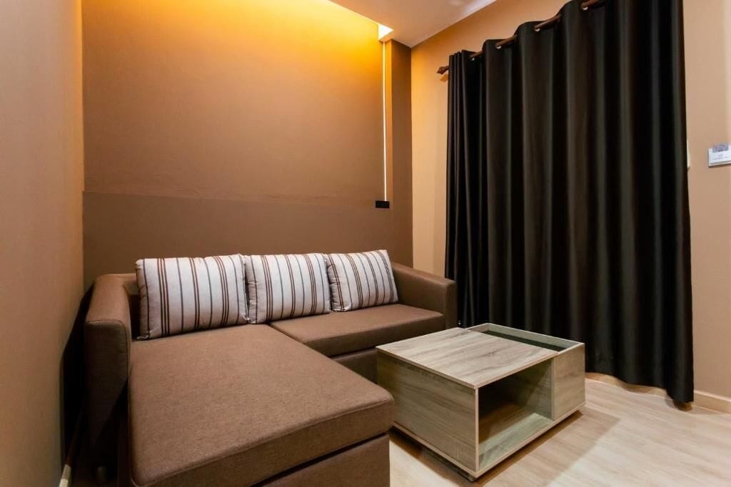 A modern living room with a sectional sofa, a wooden coffee table, and a black curtain.