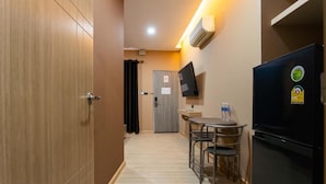 Una kitchenette funcional con refrigerador, una mesa pequeña con sillas y un televisor montado en la pared.