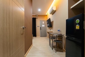 A compact kitchen area with a refrigerator, a small table with chairs, and a television mounted on the wall.