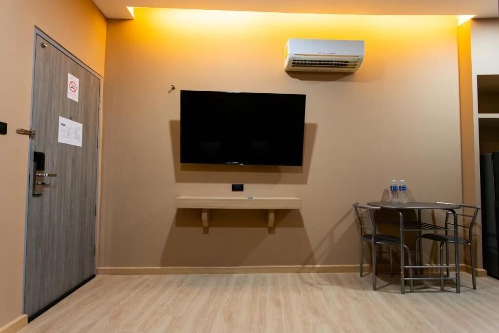 Habitación de hotel con televisor de pantalla plana montado en la pared, una mesita con sillas y un equipo de aire acondicionado.