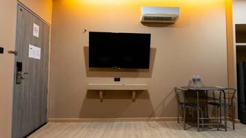 Habitación de hotel con televisor de pantalla plana montado en la pared, una mesita con sillas y un equipo de aire acondicionado.