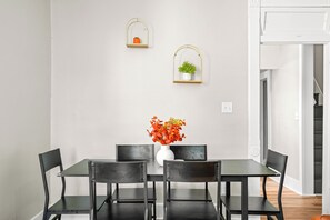 A dining area with a table and chairs, a vase with flowers, and two wall-mounted shelves with plants. - Roadmap Lodging: 2BR, Pets OK, Near the Hospital (Columbus)