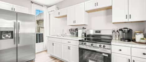 A modern kitchen with white cabinets, stainless steel appliances, and a wooden floor.