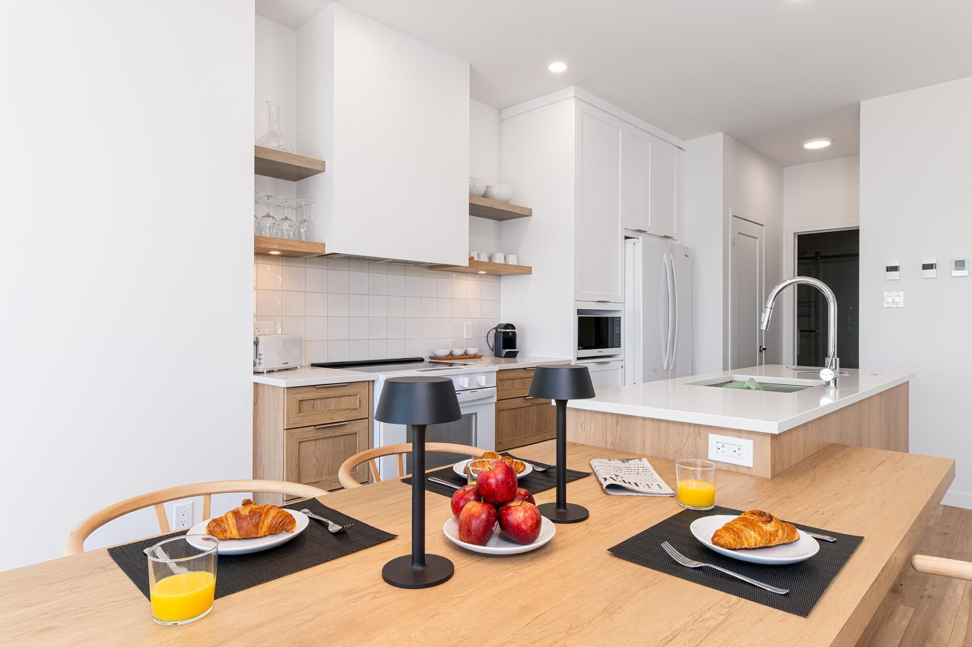 A modern kitchen with white cabinets, a central island with a sink, and a dining area with breakfast items.