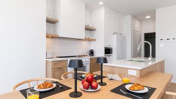 A modern kitchen with white cabinets, a central island with a sink, and a dining area with breakfast items.