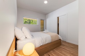 A bedroom with a bed, a bedside lamp, a window with a view, and a door. - Le Grand Bleu 1263: Private, River Sunrise (Petite-Rivière-Saint-François)