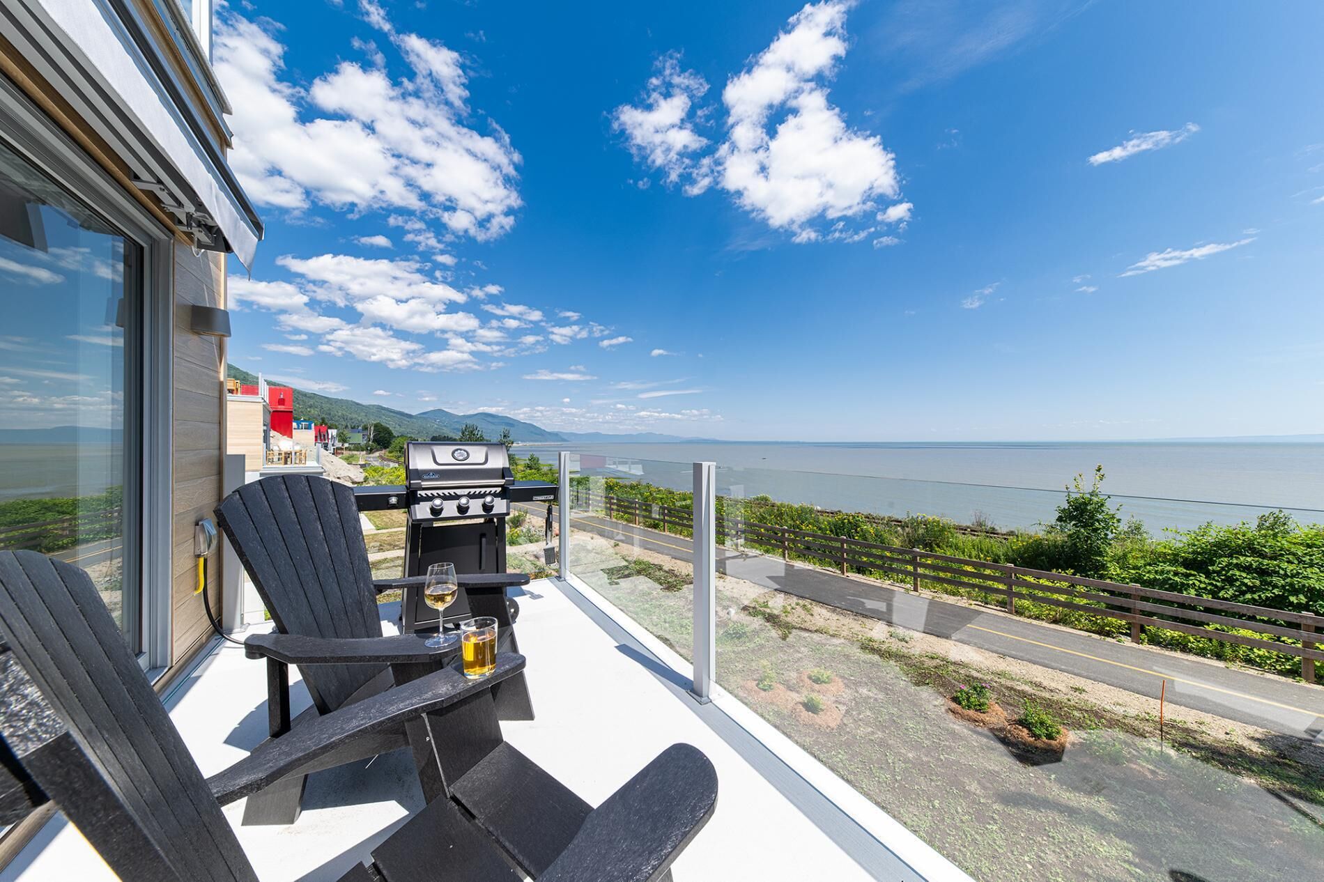 A balcony with two Adirondack chairs, a grill, and a glass of beer.