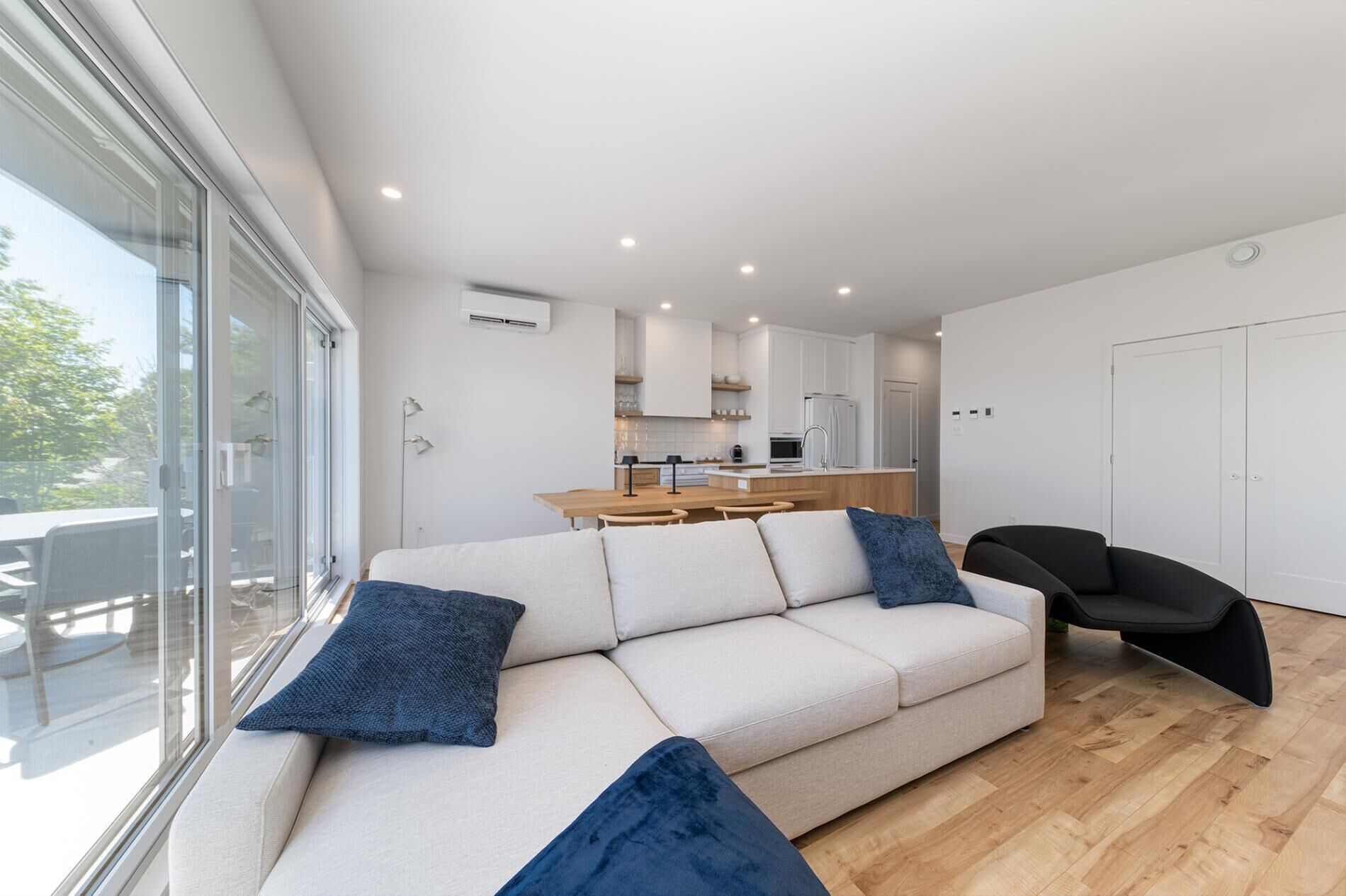 A modern living room with a sofa, a dining table, and a kitchen in the background.