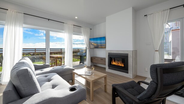 Ett modernt vardagsrum med en öppen spis, en soffa, ett soffbord och utsikt över havet.