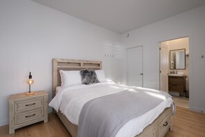 Une chambre à coucher comprenant un lit, une table de chevet et une commode. Une porte donne accès à la salle de bain.