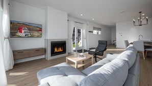 Ett modernt vardagsrum med en öppen spis, en stor grå soffa och en matplats med ett bord och stolar.