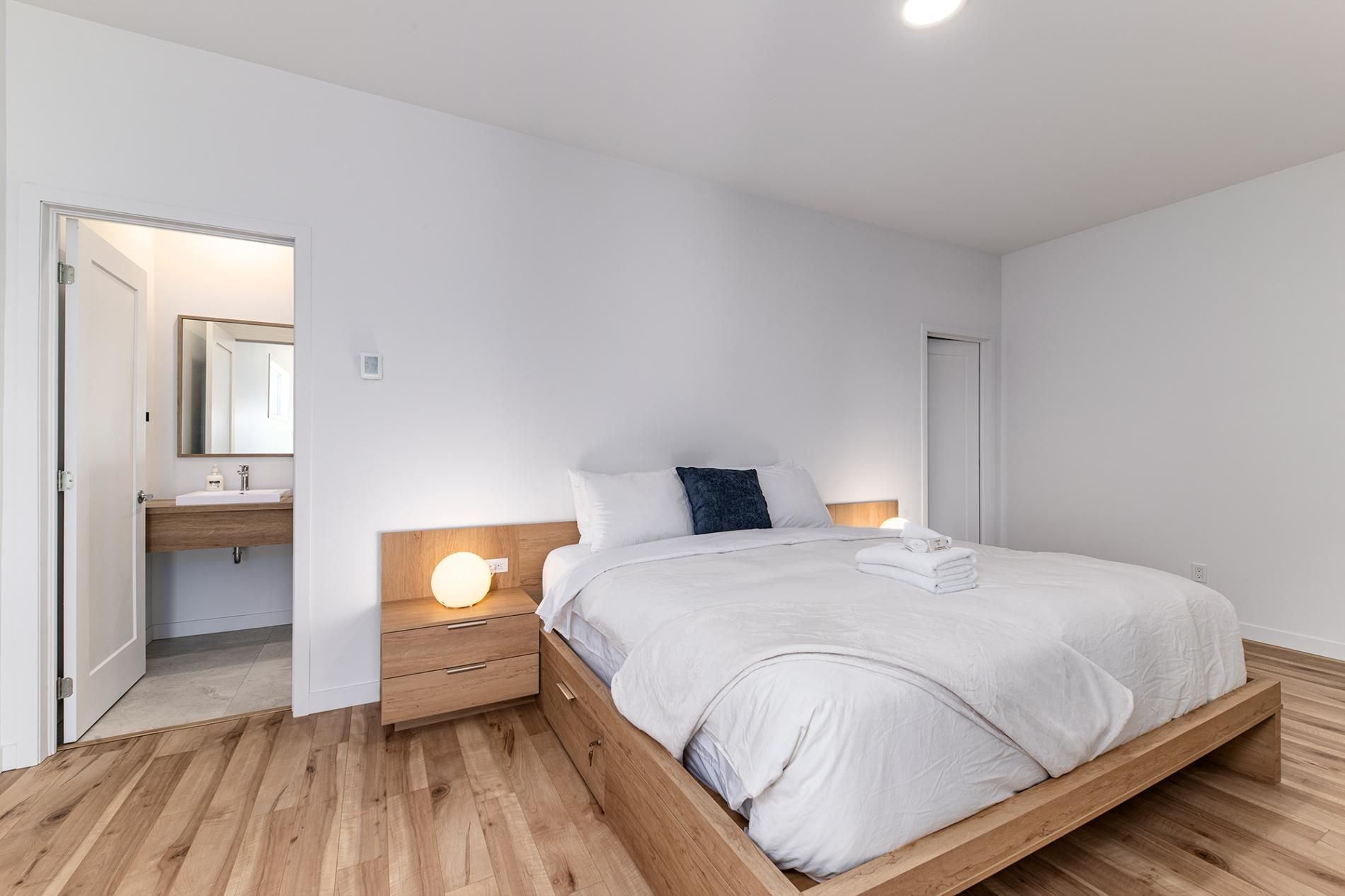 A minimalist bedroom with a bed, bedside table, and a nightstand with a lamp.
