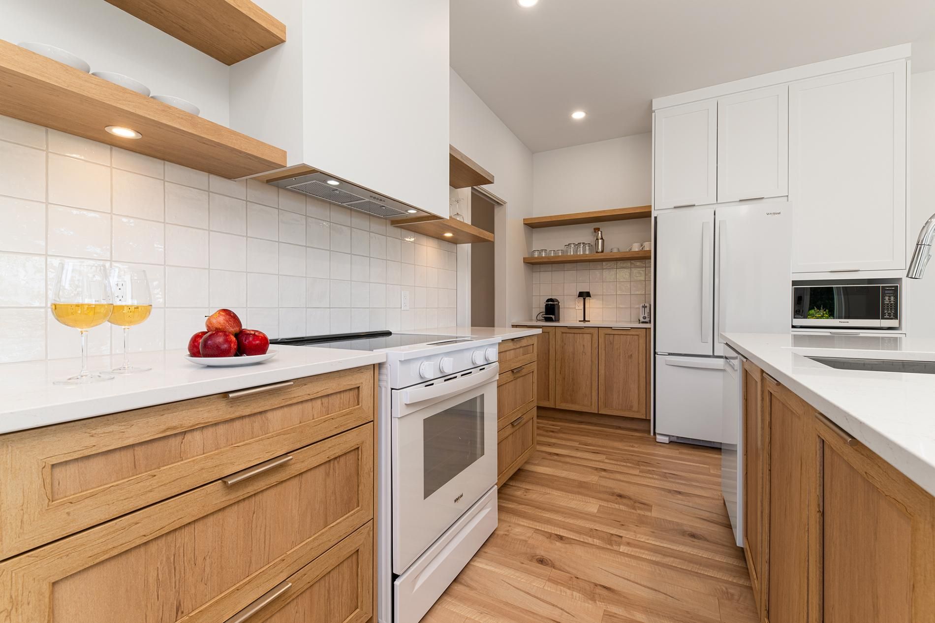 A modern kitchen with white cabinetry, a white countertop, wooden flooring, and a built-in oven.