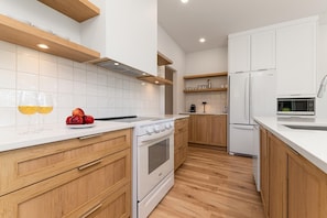 Una cocina moderna con armarios blancos, encimera blanca, suelo de madera y horno integrado.